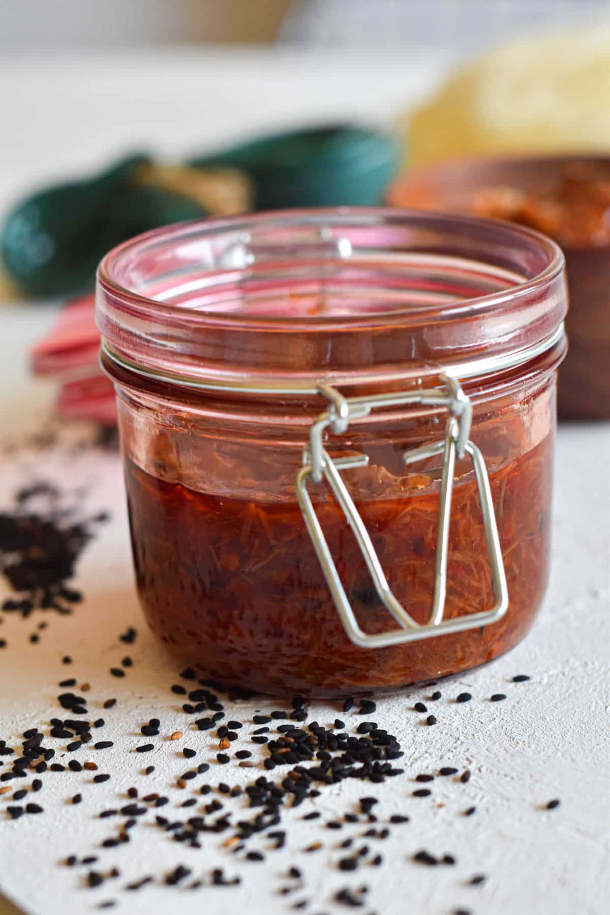 XO sauce in a jar on white background with black sesame seeds scattered around.