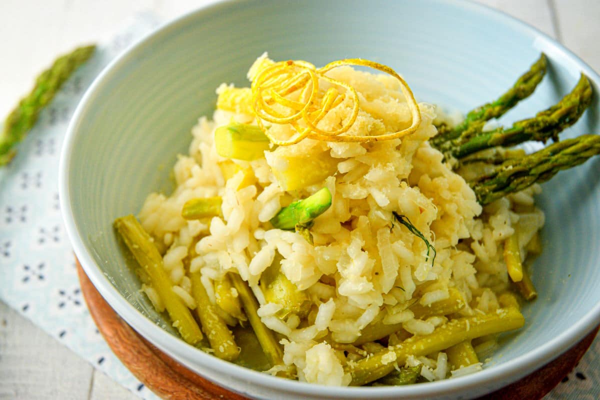 Risotto with lemon zest and green asparagus in light blue bowl.