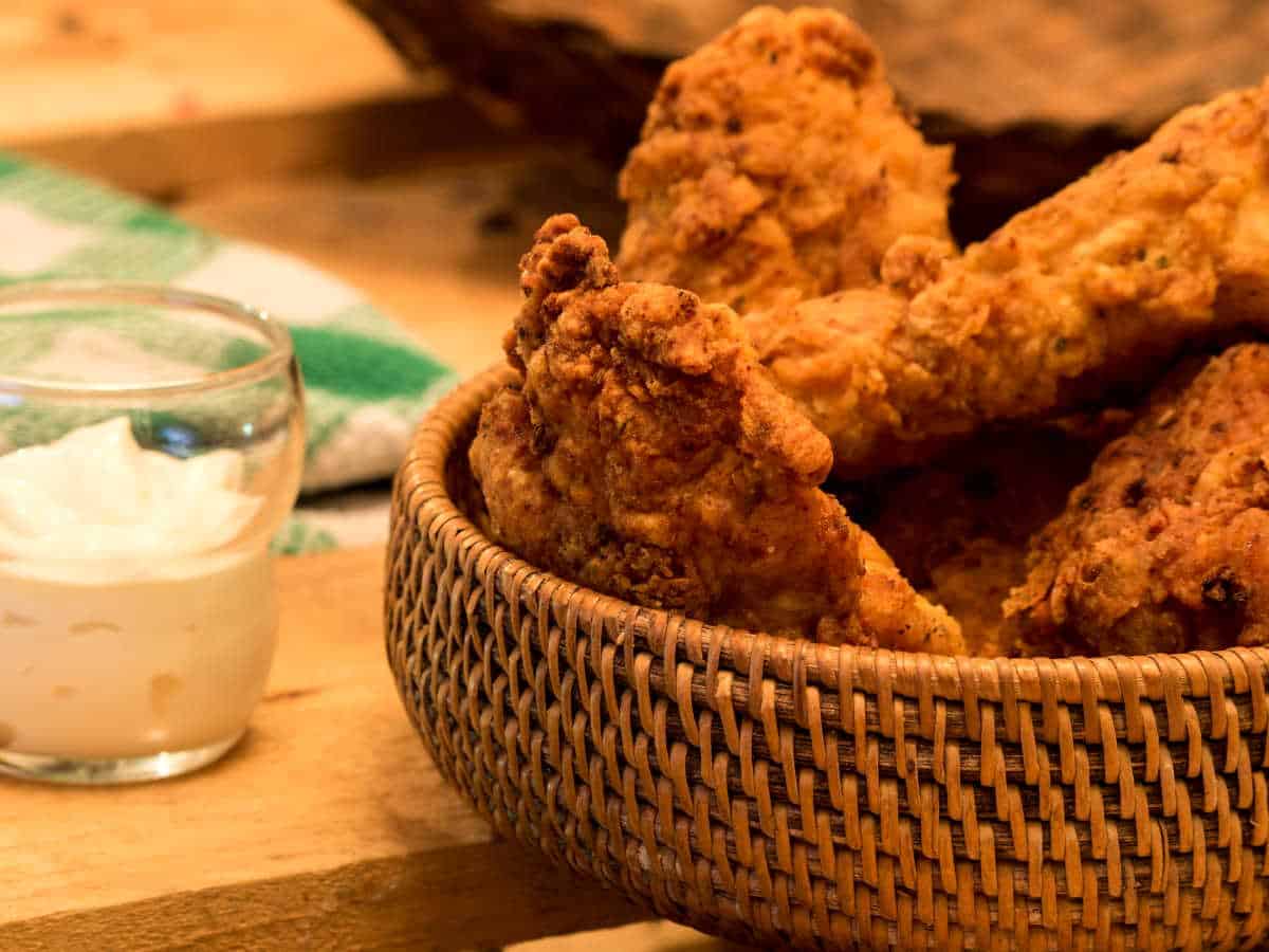 Electric skillet fried chicken in weaved basket.