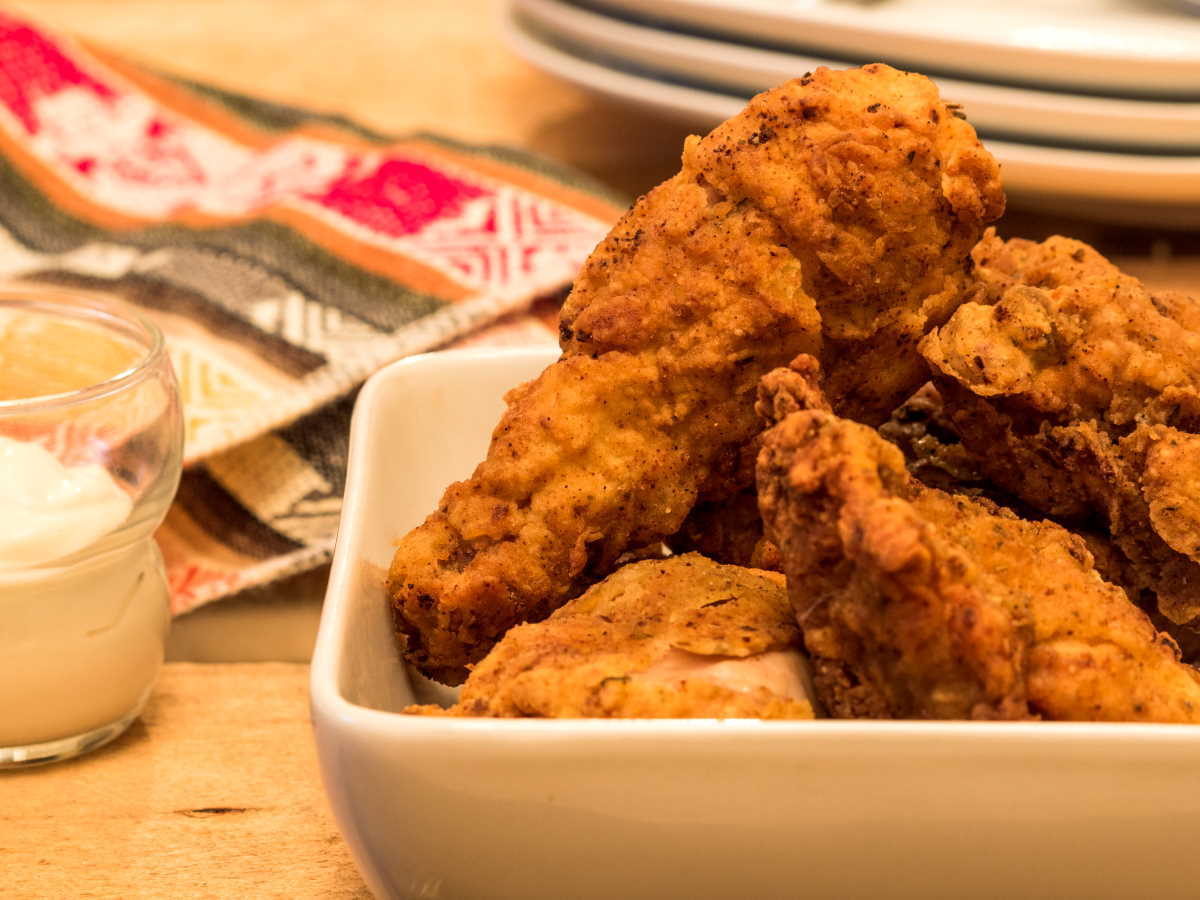 Electric skillet fried chicken in porcelain dish with garlic mayo on the side.