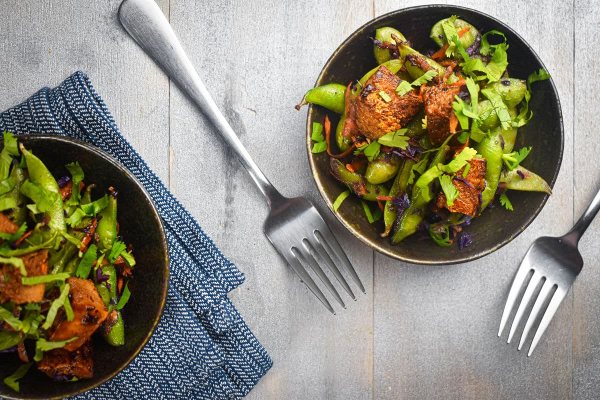 Fried tofu and snap peas in bowls with forks.