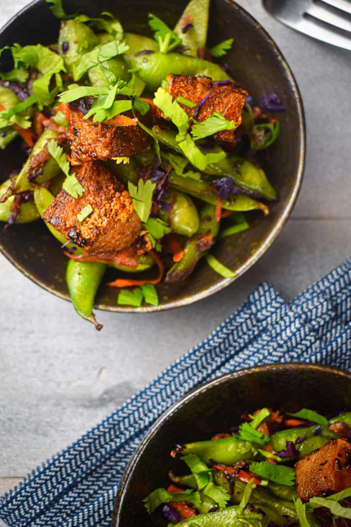 Fried tofu with snap peas, red cabbage and fresh cilantro in bowls.