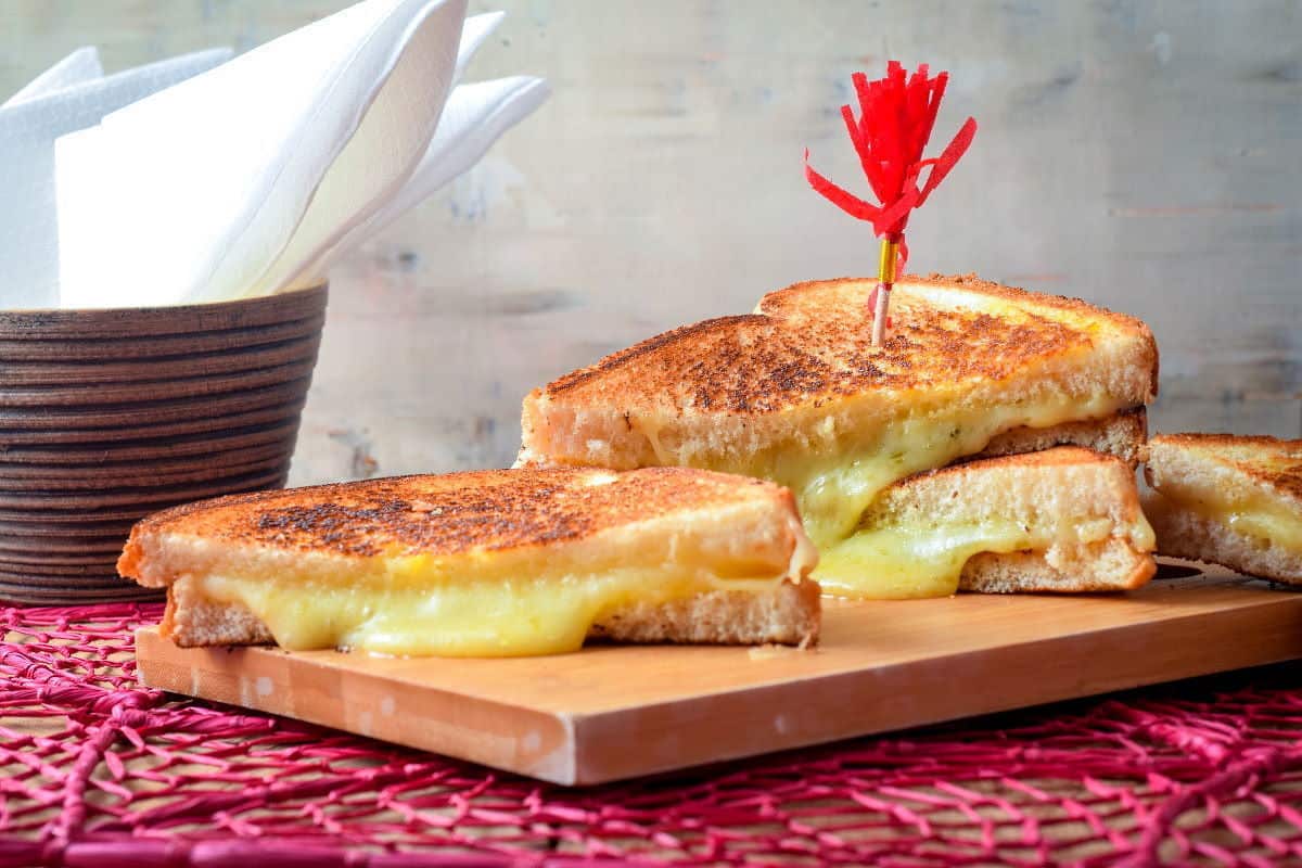 Electric skillet grilled cheese sandwiches on a cutting board over a pink doiley.
