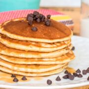 Pancakes piled on a plate with chocolate chips and maple syrup.
