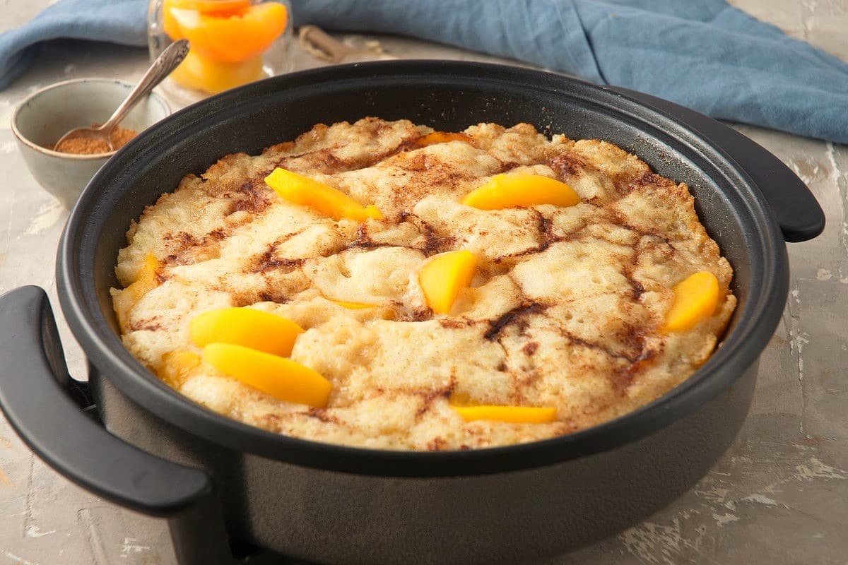 Peach cobbler in an electric skillet on grey background.