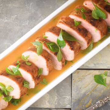 Sliced pork tenderloin in white serving dish with orange white wine sauce.