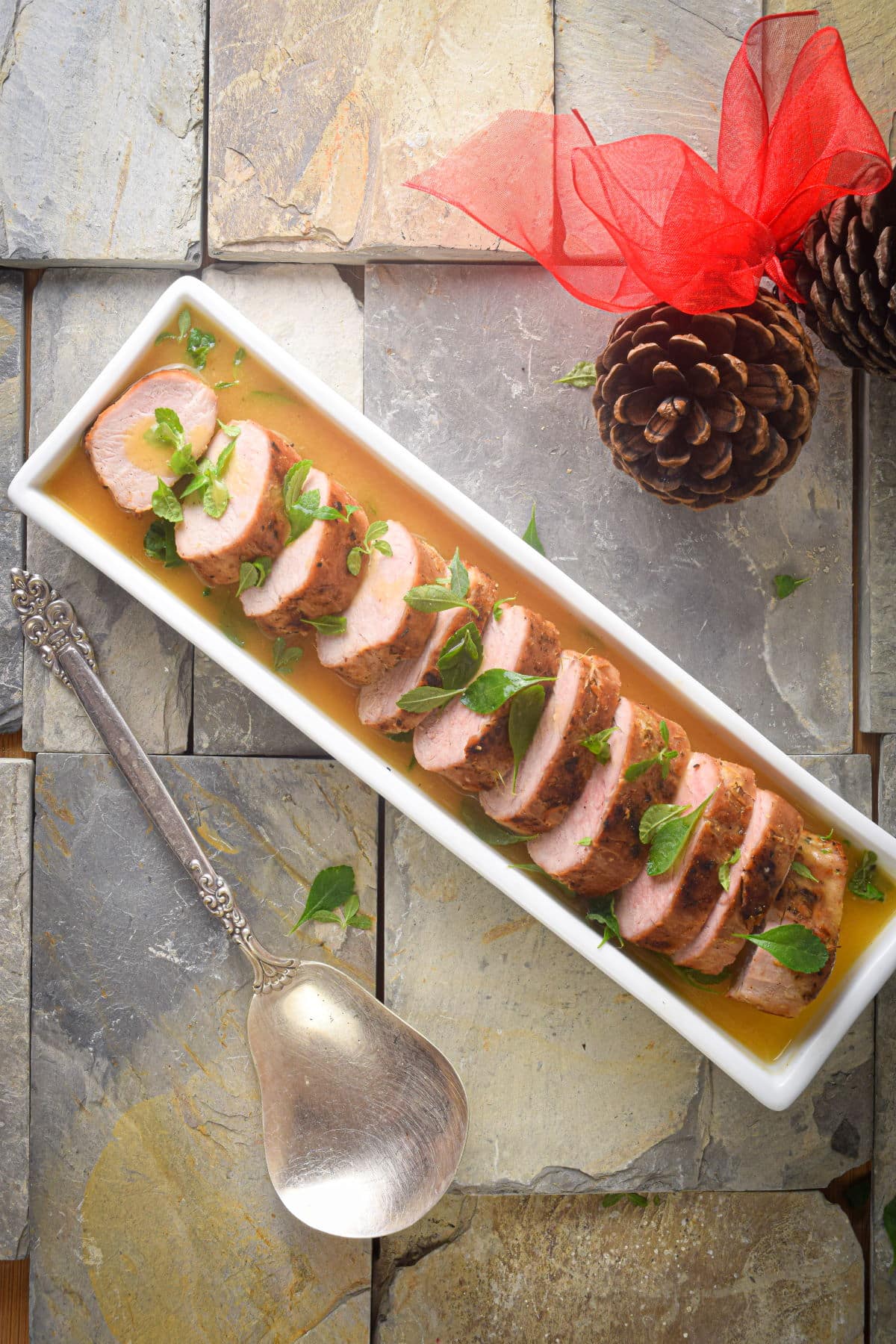 Sliced pork tenderloin in white serving dish with orange white wine sauce.