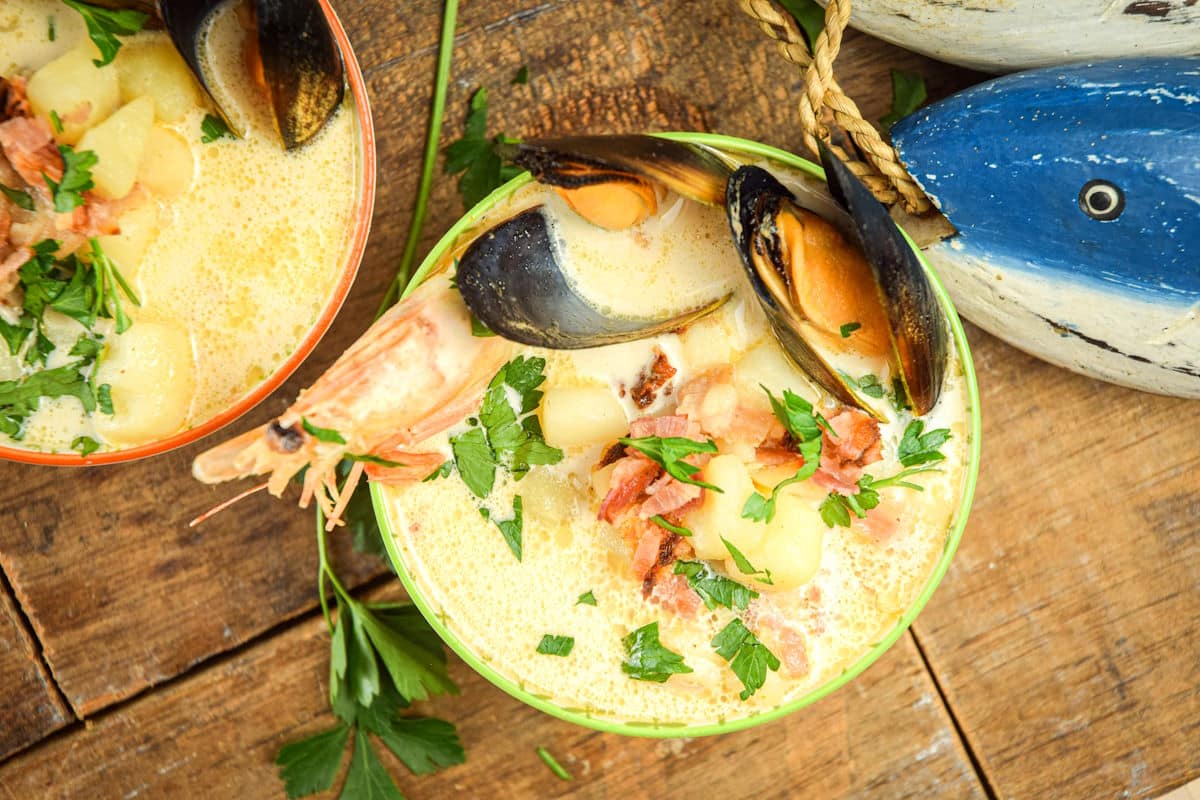 Seafood chowder in bowl with blue, wooden fish on the side.