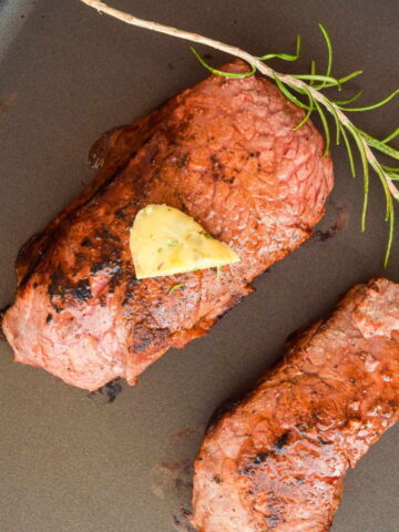 2 steaks in an electric skillet with butter and a rosemary sprig on top.