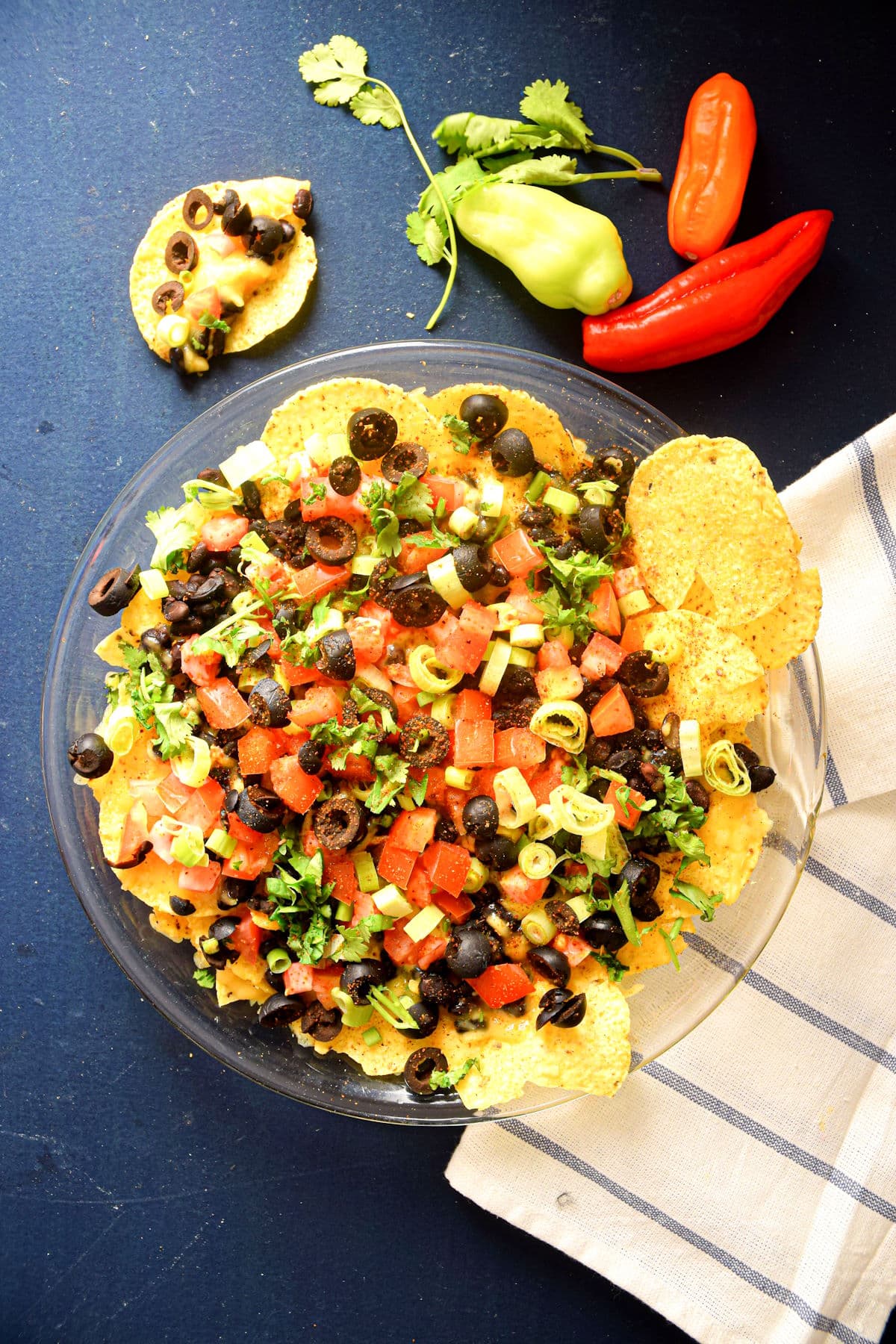 Veggie nachos on a clear glass plate on blue background.
