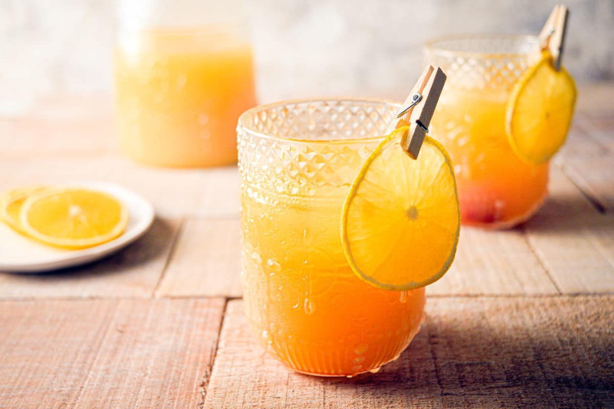 Fall Pumpkin Party Punch in a clear glass with a thin orange slice garnish clipped on with a clothespin.
