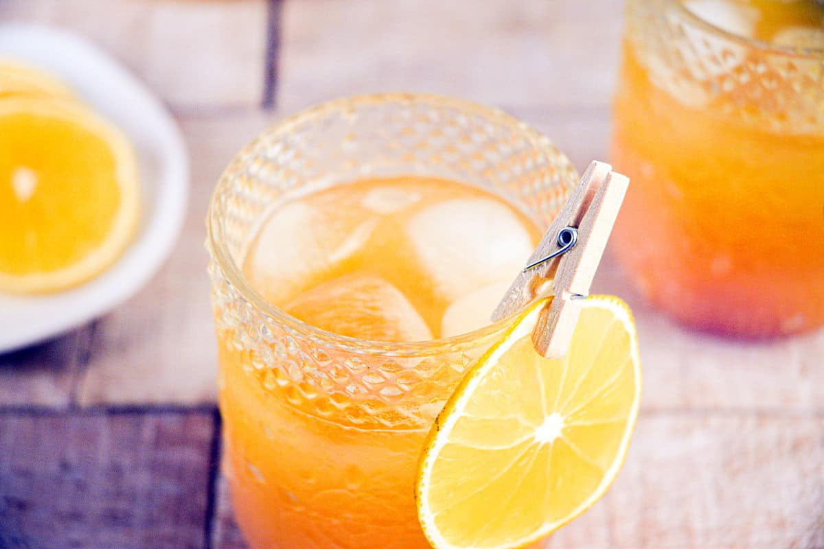 Fall Pumpkin Party Punch in a clear glass with ice and orange slice garnish.