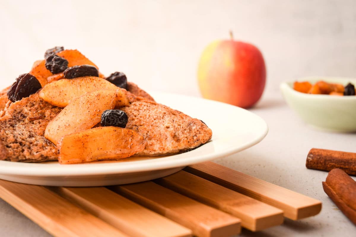 French toast with sliced apples and raisins on white plate.
