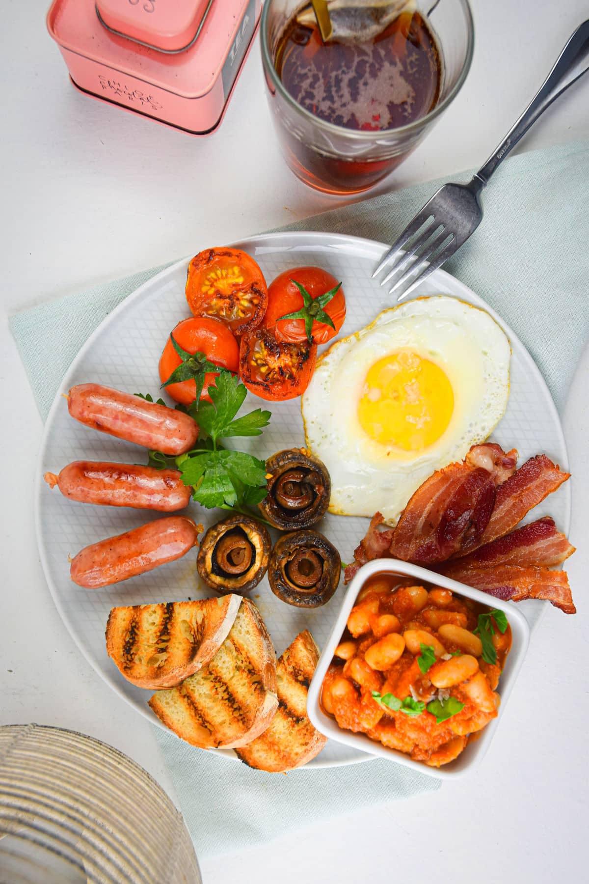Full English breakfast on white plate with a fork and tea cup on the side.