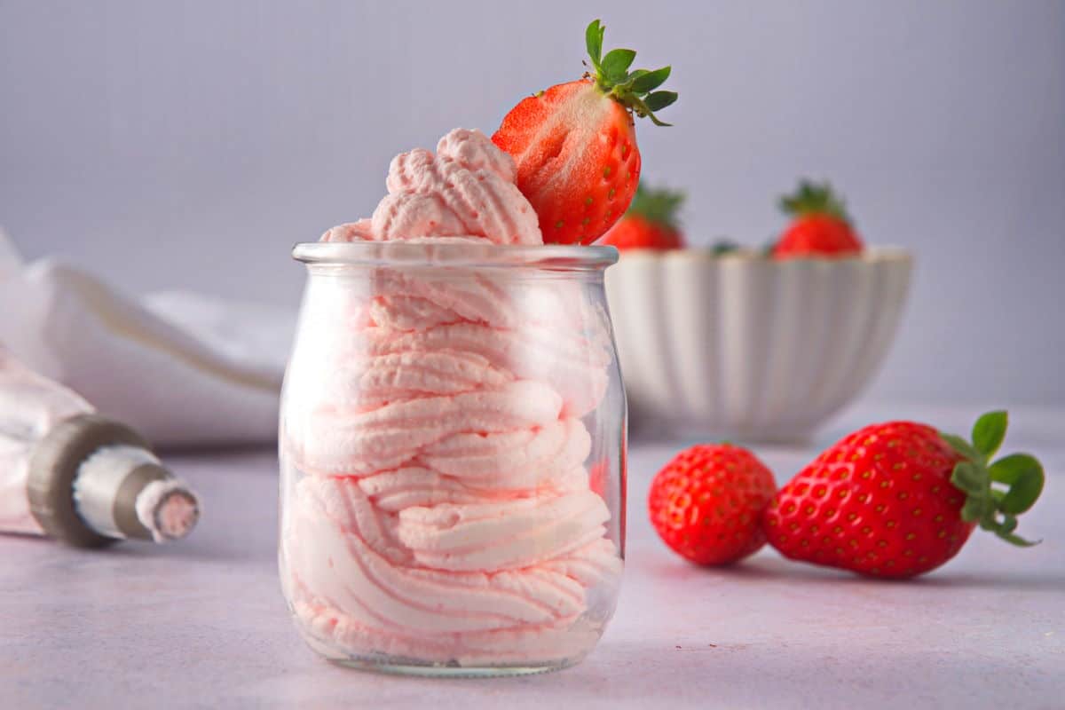Grenadine whipped cream in glass jar with fresh strawberries and a piping bag on the side.