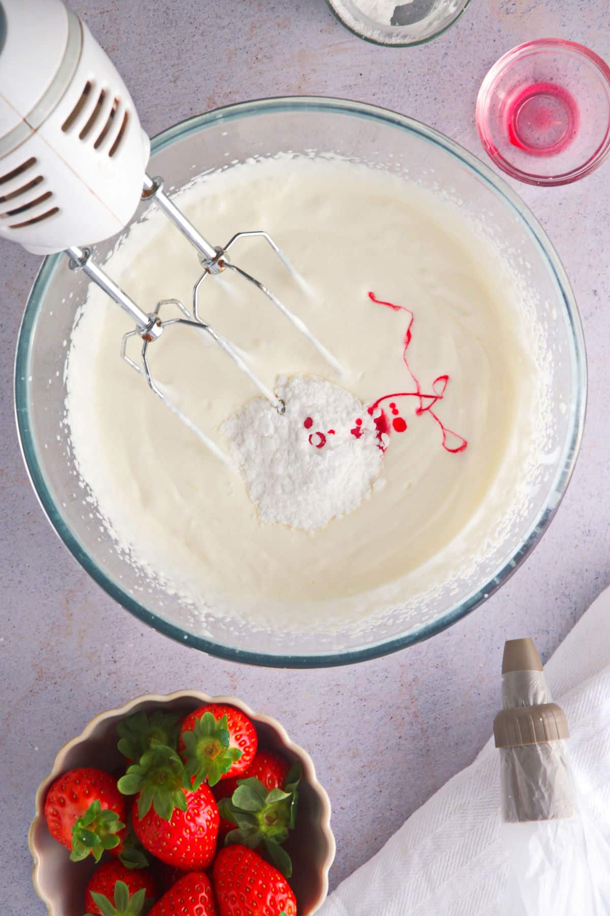 A bowl of heavy cream, icing sugar and grenadine and an electric hand mixer.
