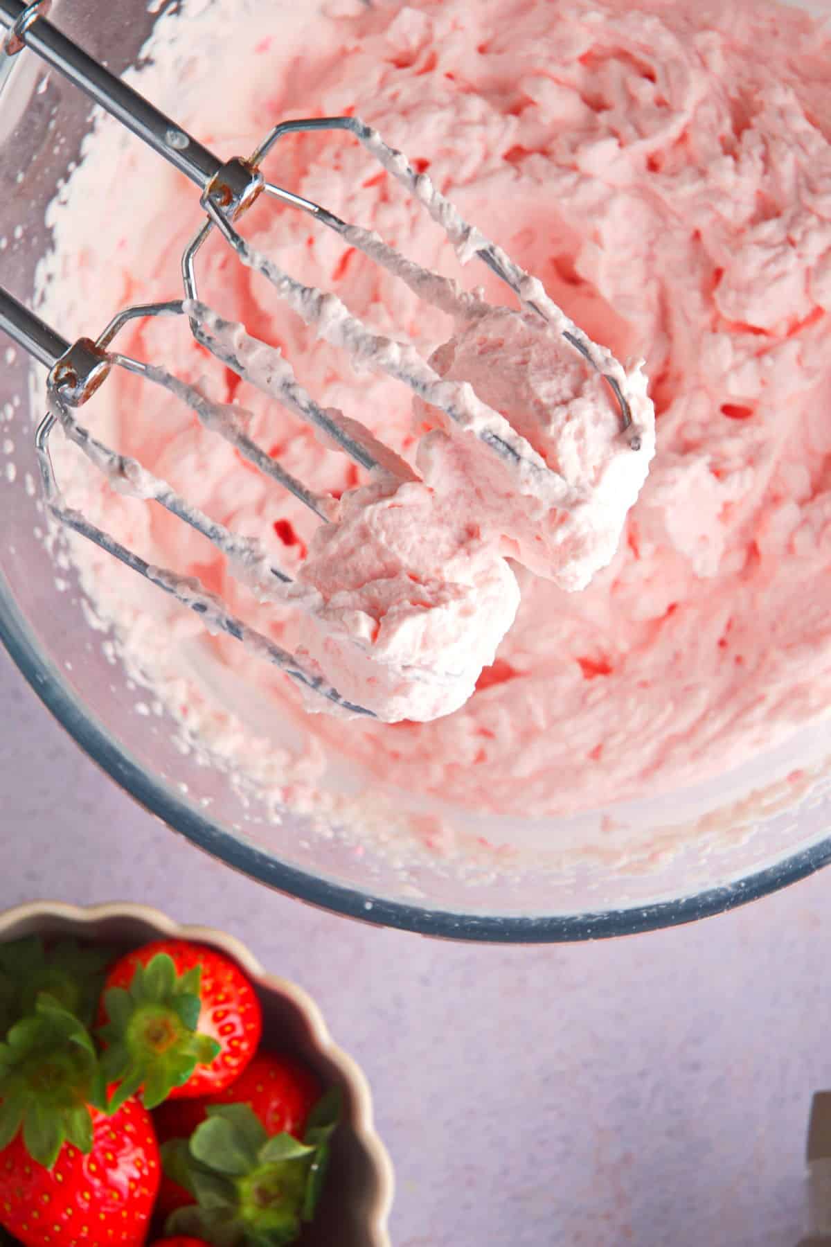 A bowl of grenadine whipped cream with beaters and fresh strawberries on the side.