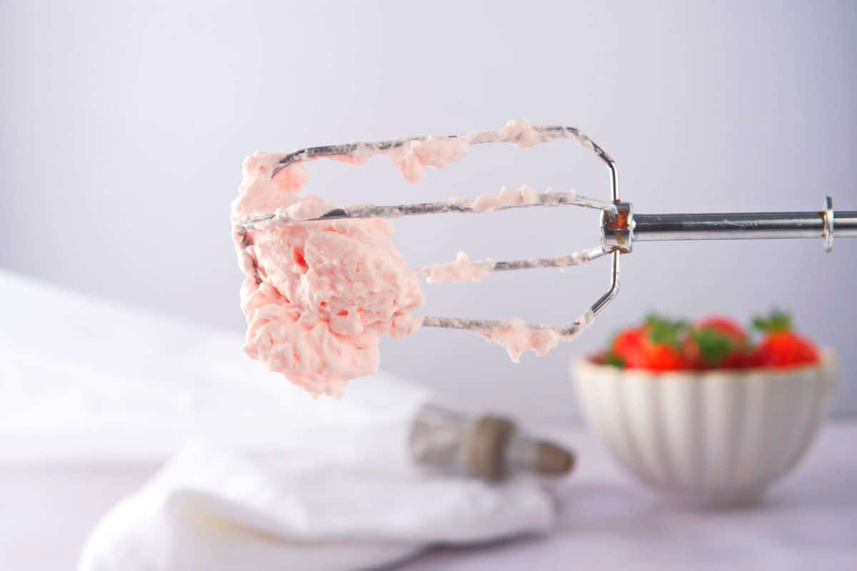 Metal whisk attachment with whipped cream on it.