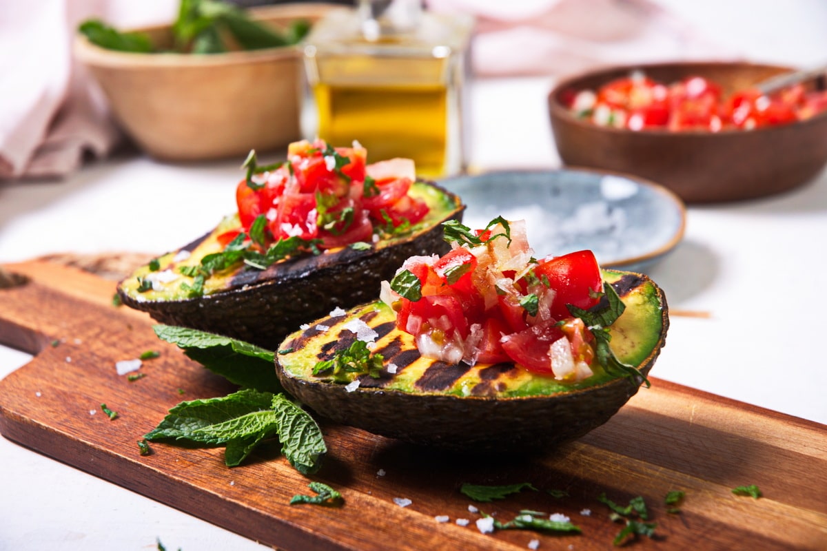 Grilled, stuffed avocados on wooden cutting board.