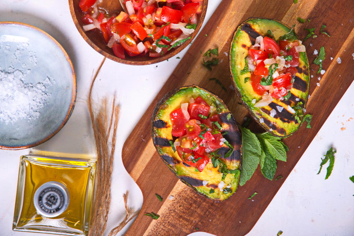 Stuffed, grilled avocadoes on wooden cutting board with olive oil and salt on the side.
