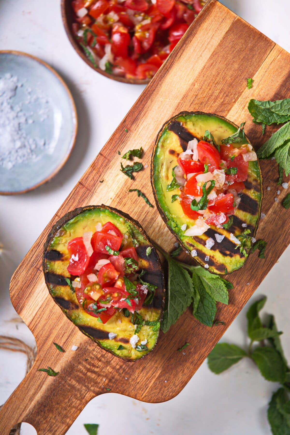 Stuffed, grilled avocadoes on wooden cutting board, sprinkled with sea salt flakes.