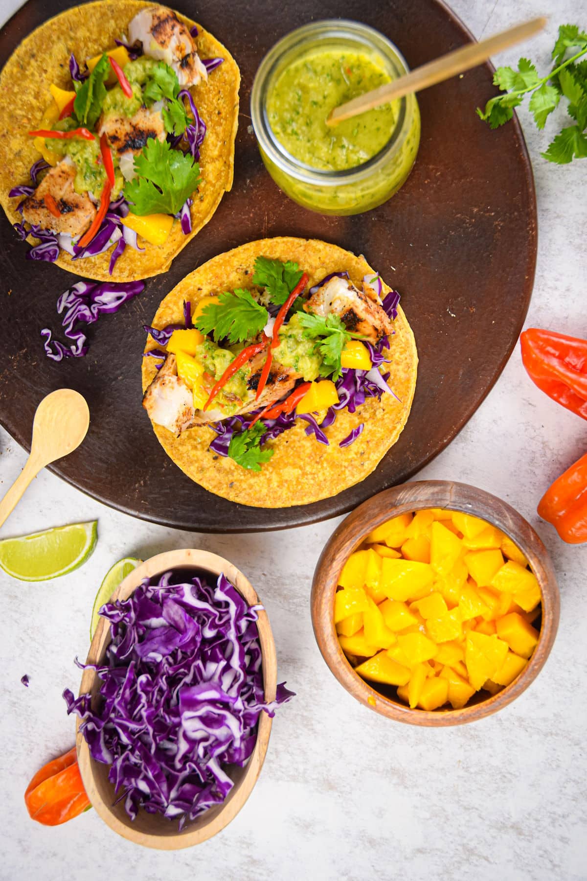 Halibut tacos on a brown serving plate with tomatillo salsa, mango, lime and red cabbage.