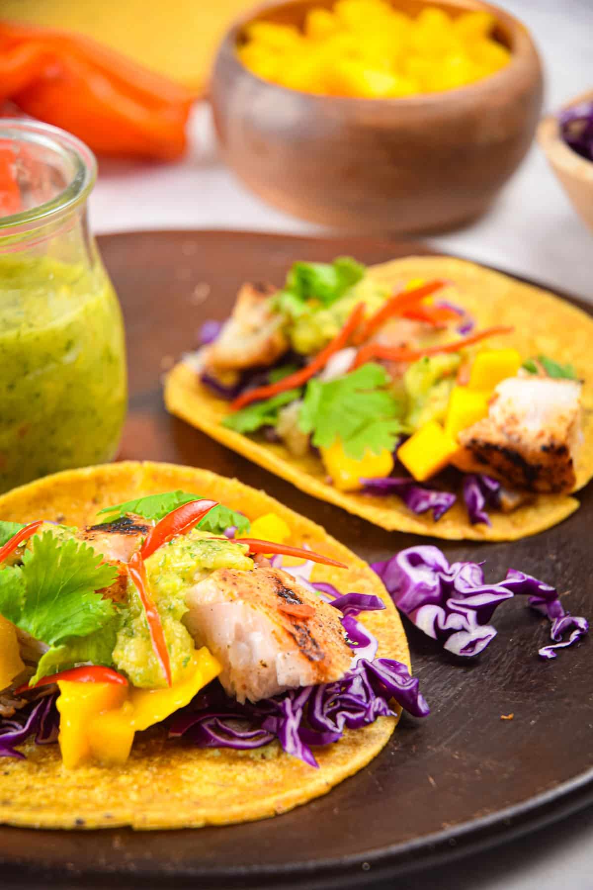 Halibut tacos on plate with green salsa on the side.