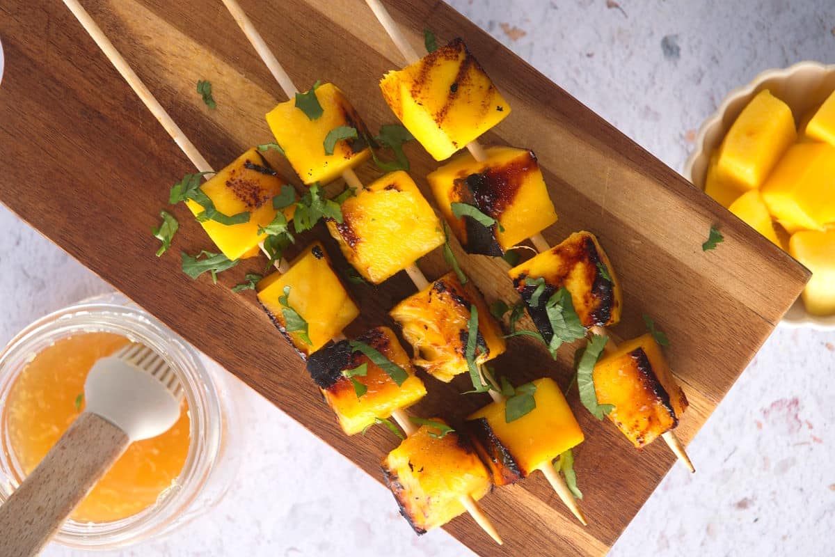 Grilled mango skewers on wooden serving board.