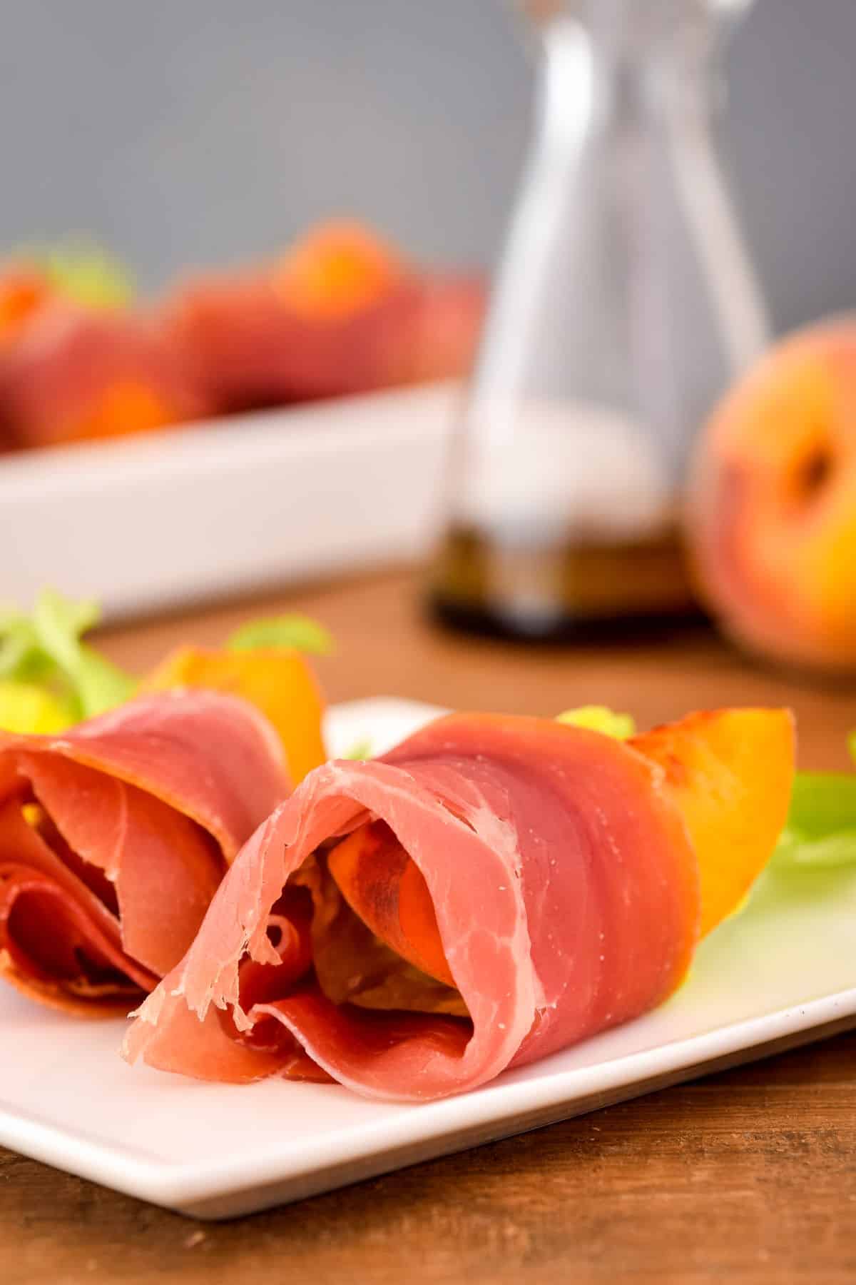 Grilled prosciutto wrapped peaches on white plate.