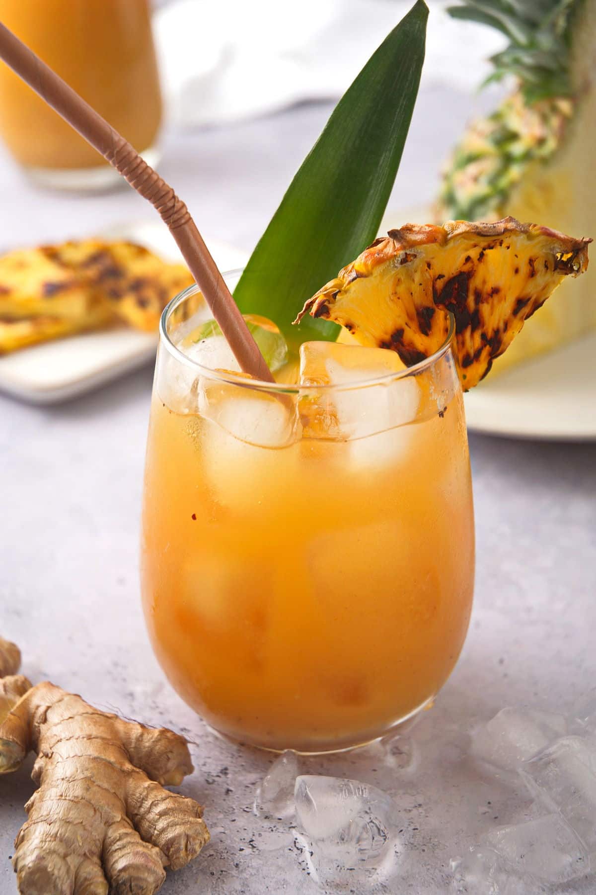 Grilled pineapple juice and wedge in glass with fresh ginger root on the side.