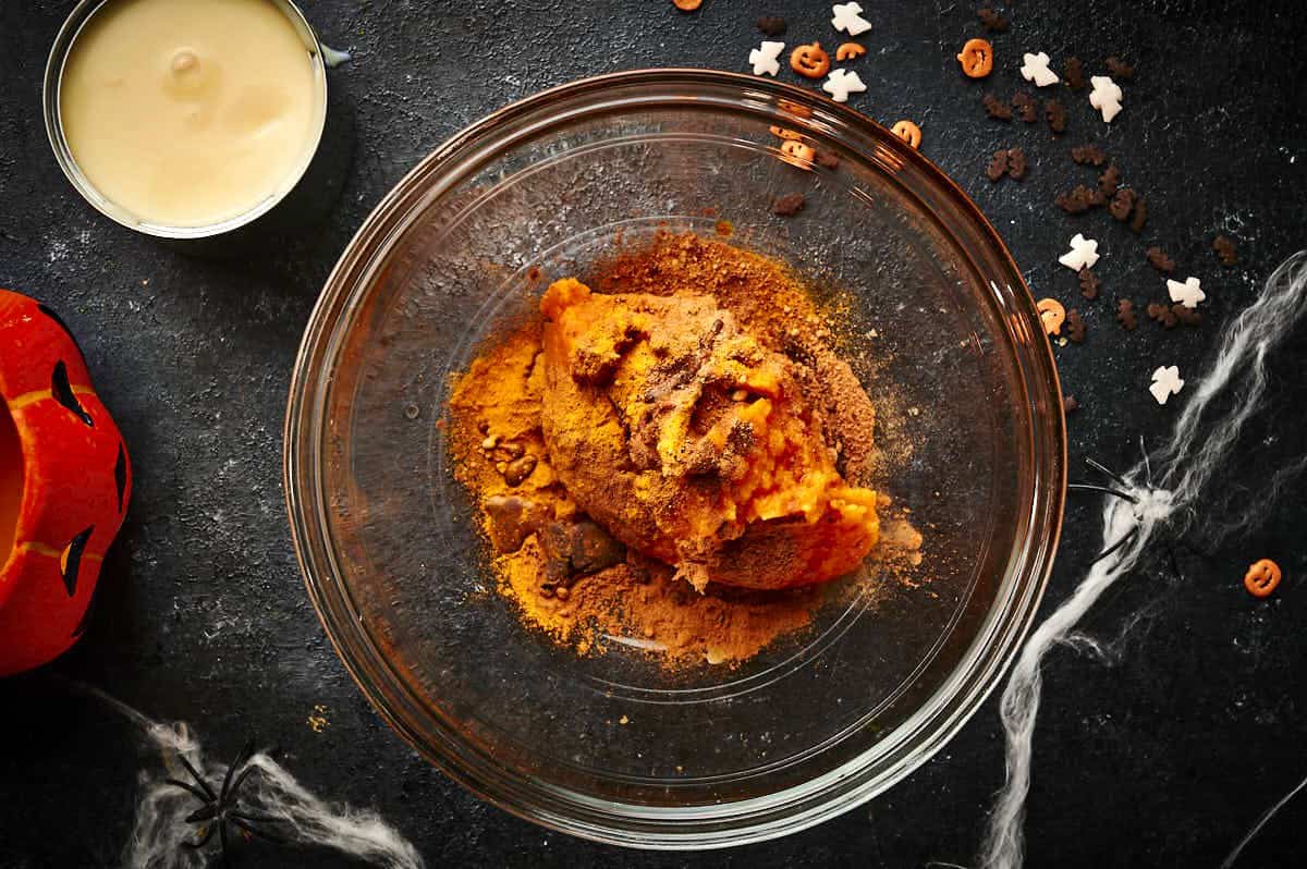 Pumpkin purée and spices in bowl on black background.
