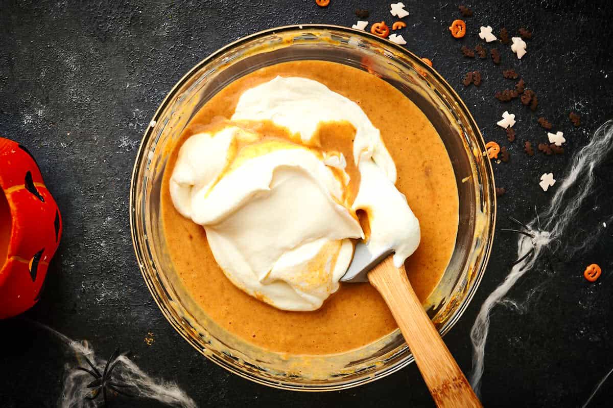Halloween ice cream mixture in bowl with spatula surrounded by Halloween decorations.