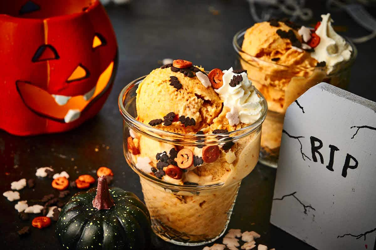 Halloween ice cream in small glass ice cream dish with whipped cream and spooky candies.