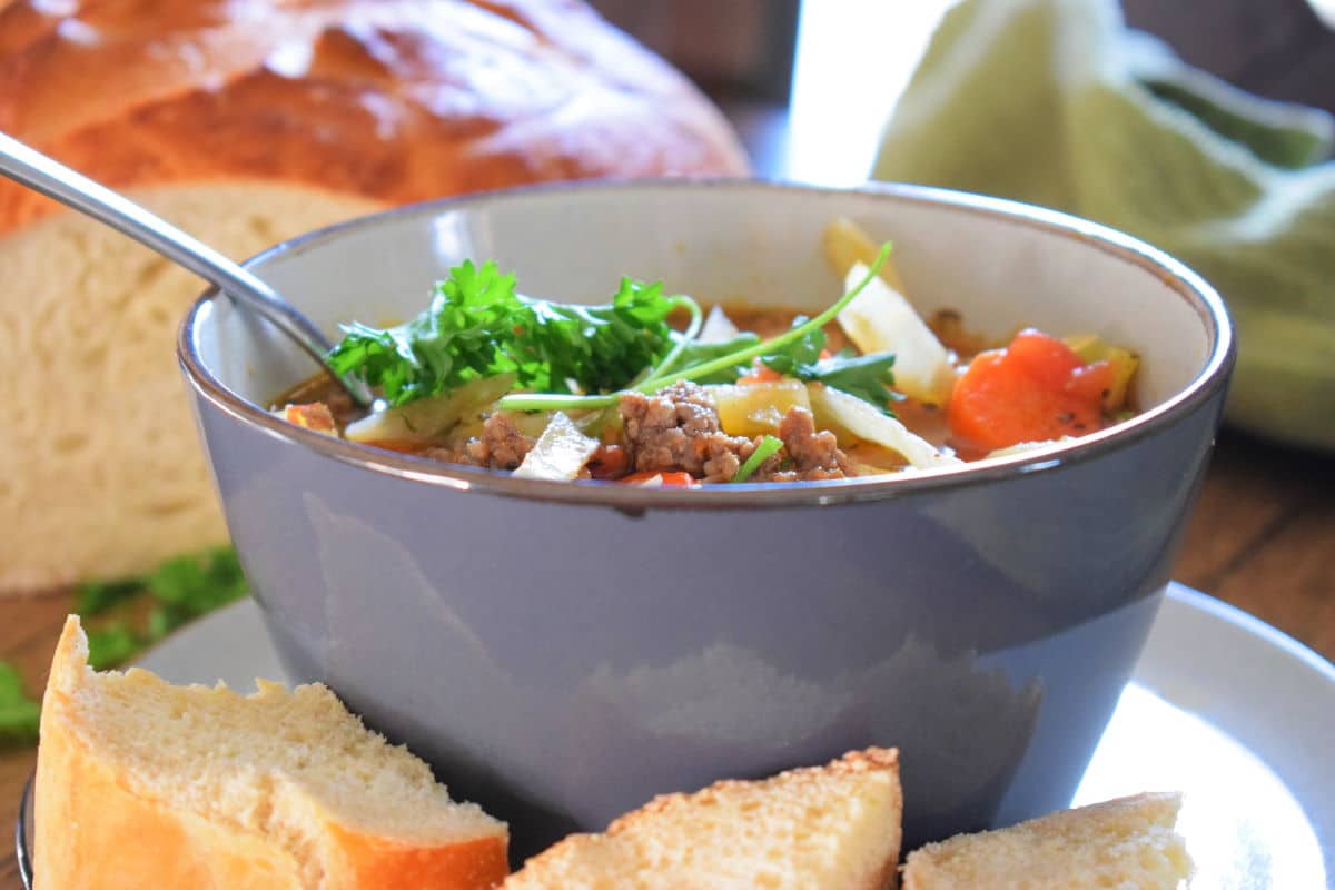 Beef and cabbage soup in a blue bowl with sourdough loaf.