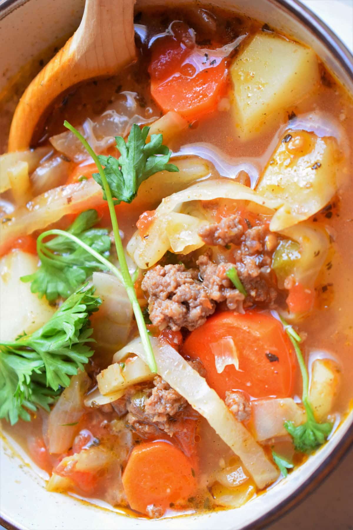 Beef and cabbage soup in a bowl with a wooden soup spoon.
