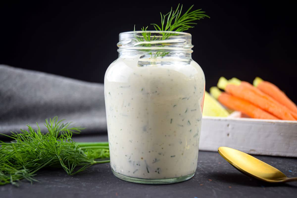 Homemade ranch dressing in a jar with fresh dill and a golden spoon on the side.