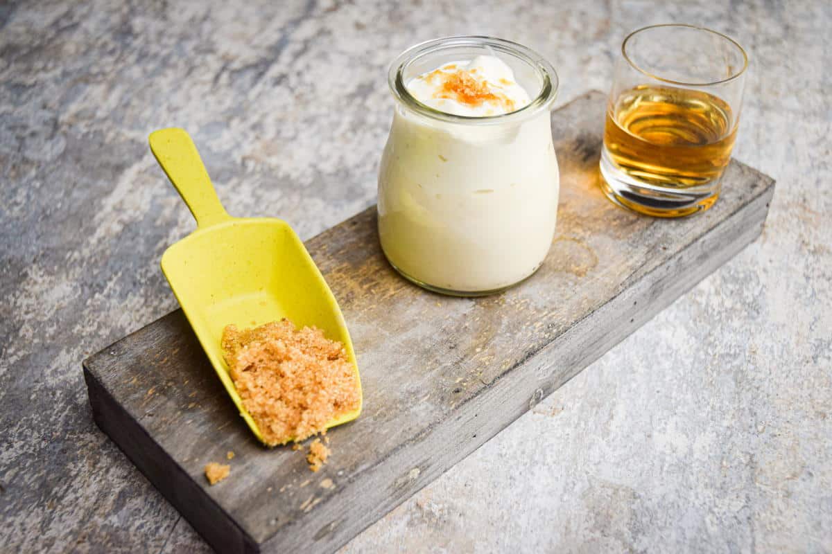 Whipped topping in a small bowl, bourbon in a small glass and a scoop of brown sugar on wooden background.