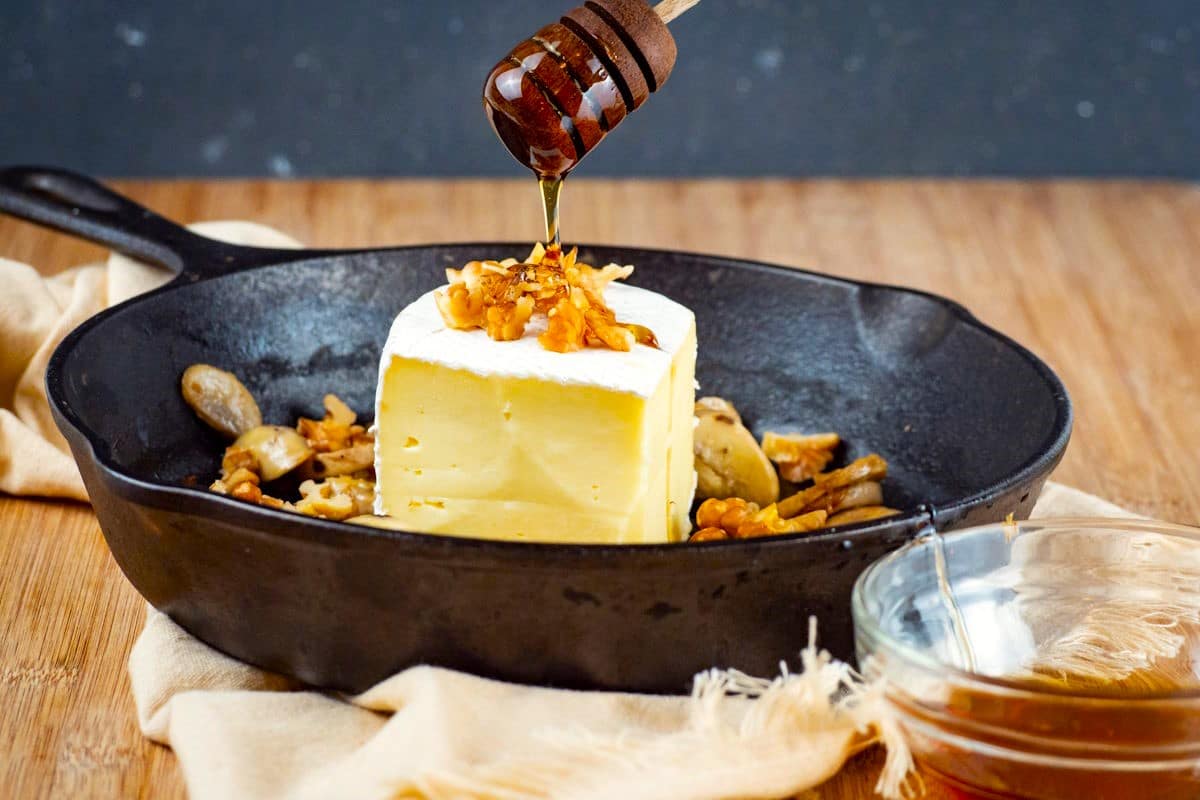 Brie wedge in cast iron pan with honey drizzling over.