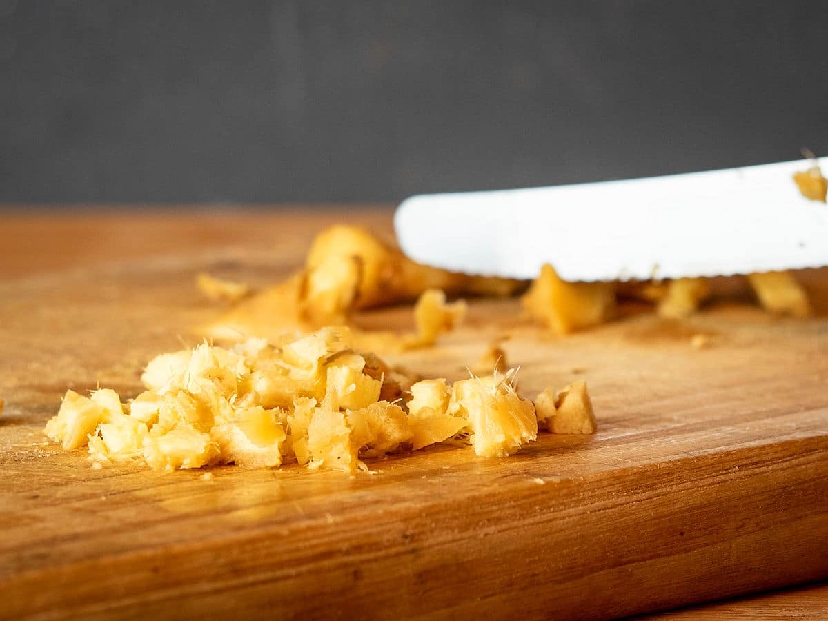 Ginger root chopped on cutting board with knife.