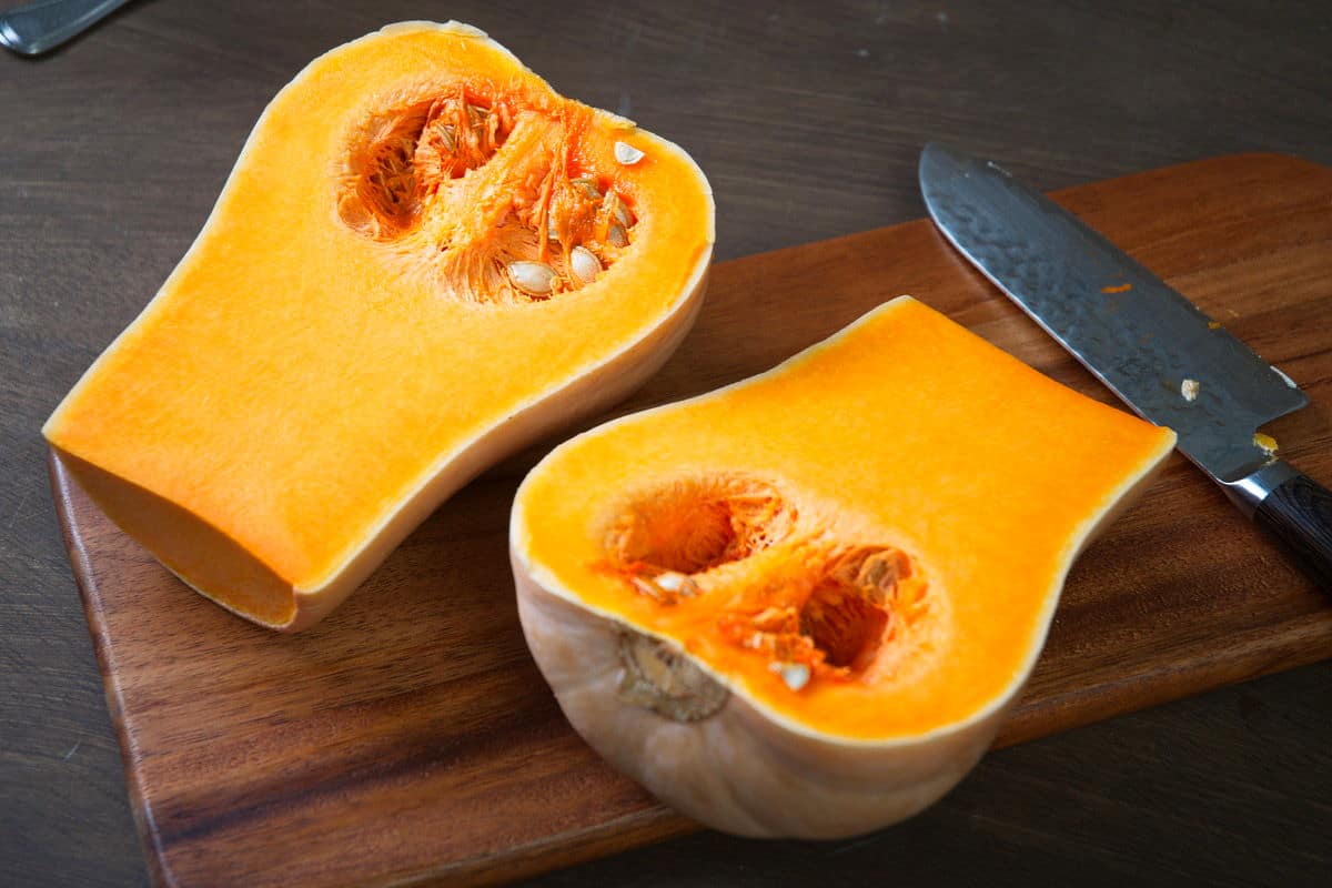 Sliced open butternut squash on wooden cutting board with a chef's knife.