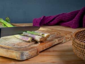 Asparagus stems getting gut off with knife on cutting board.
