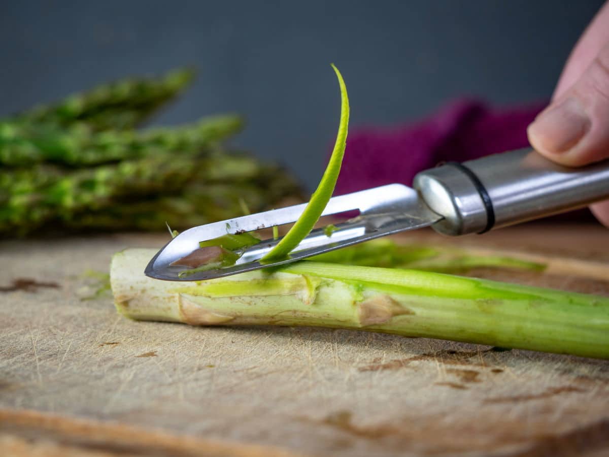 How to Cook Asparagus on the Stove - Step 3 Asparagus stems getting peeled on wooden cutting board.