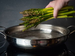 Adding asparagus stems to pan with boiling water.