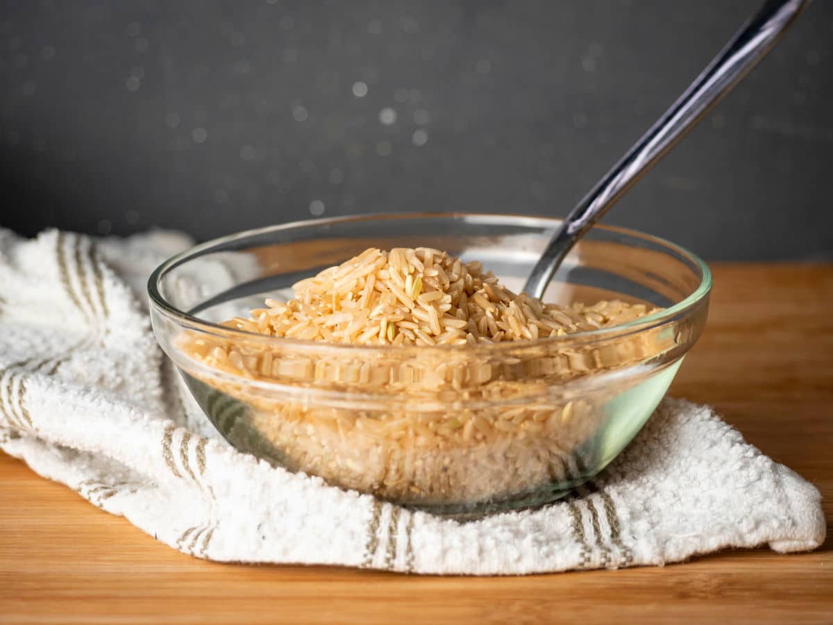 Dry brown rice in clear bowl with a spoon.