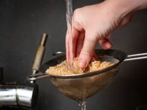 Brown rice in sieve with water running over it.