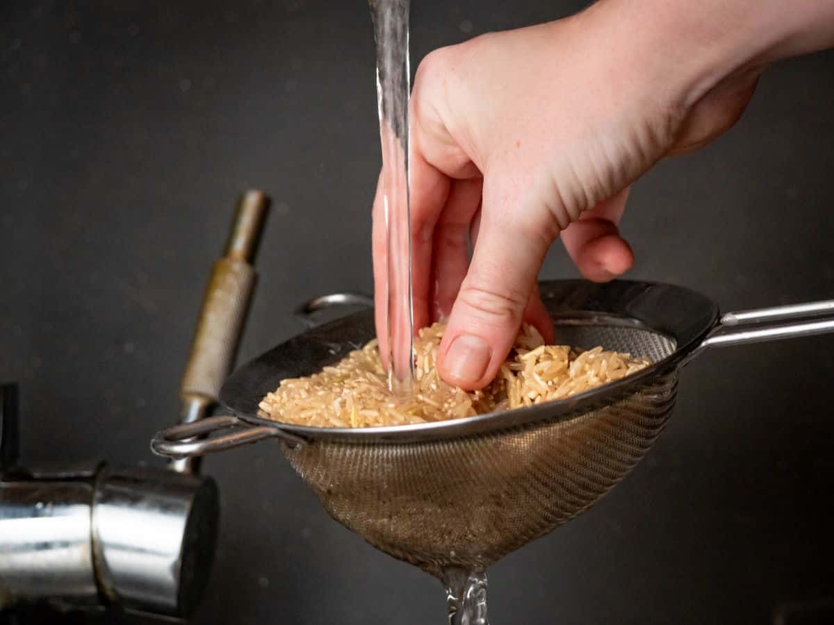 Brown rice in sieve with water running over it.