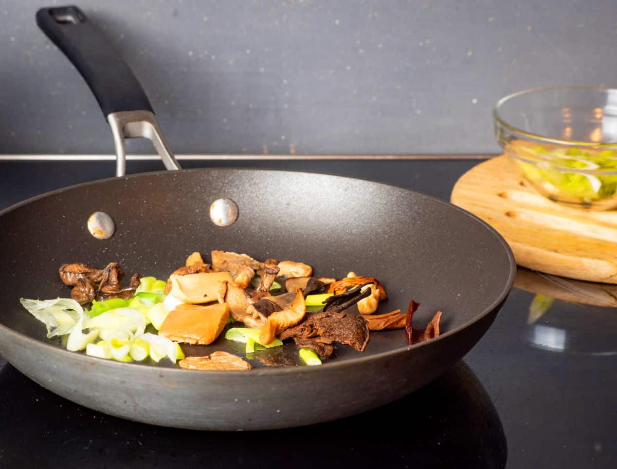 Mushrooms and green onions in frying pan.