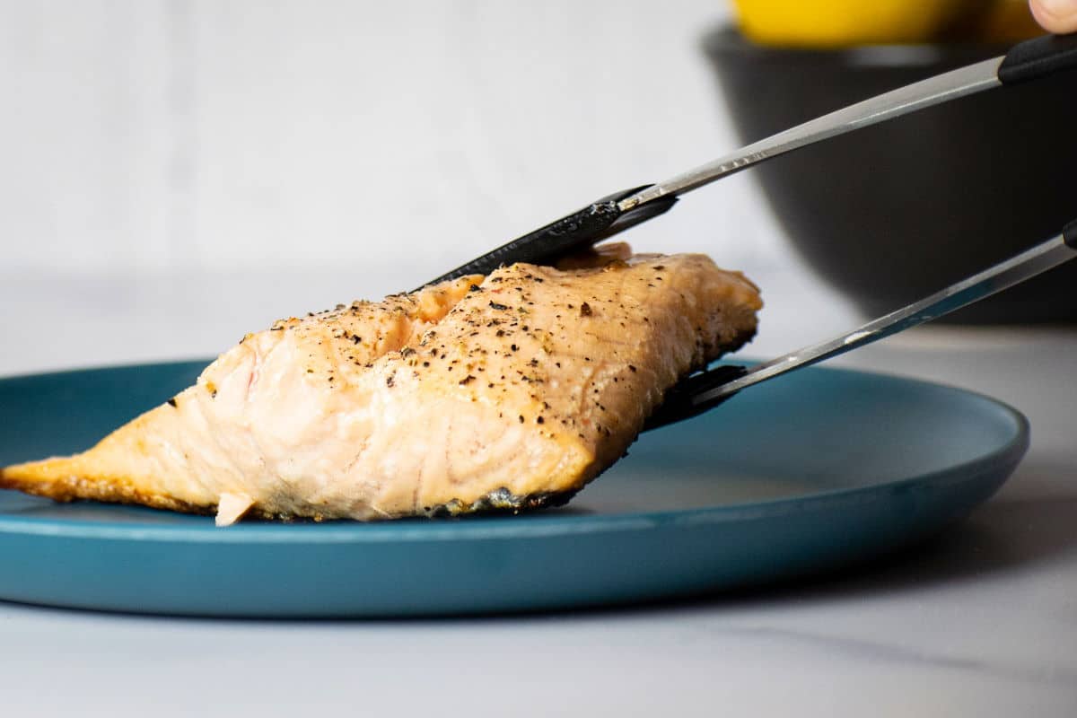Salmon fillet in between tongs on blue plate.