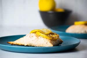 Cooked salmon fillet with lemon slices on blue plate.