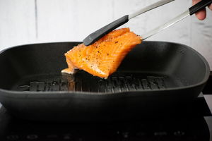 Salmon fillet in tongs over grill pan.